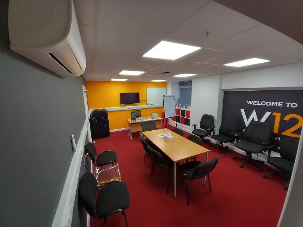 Conference room with central table, bright orange wall, ideal for meetings and events.