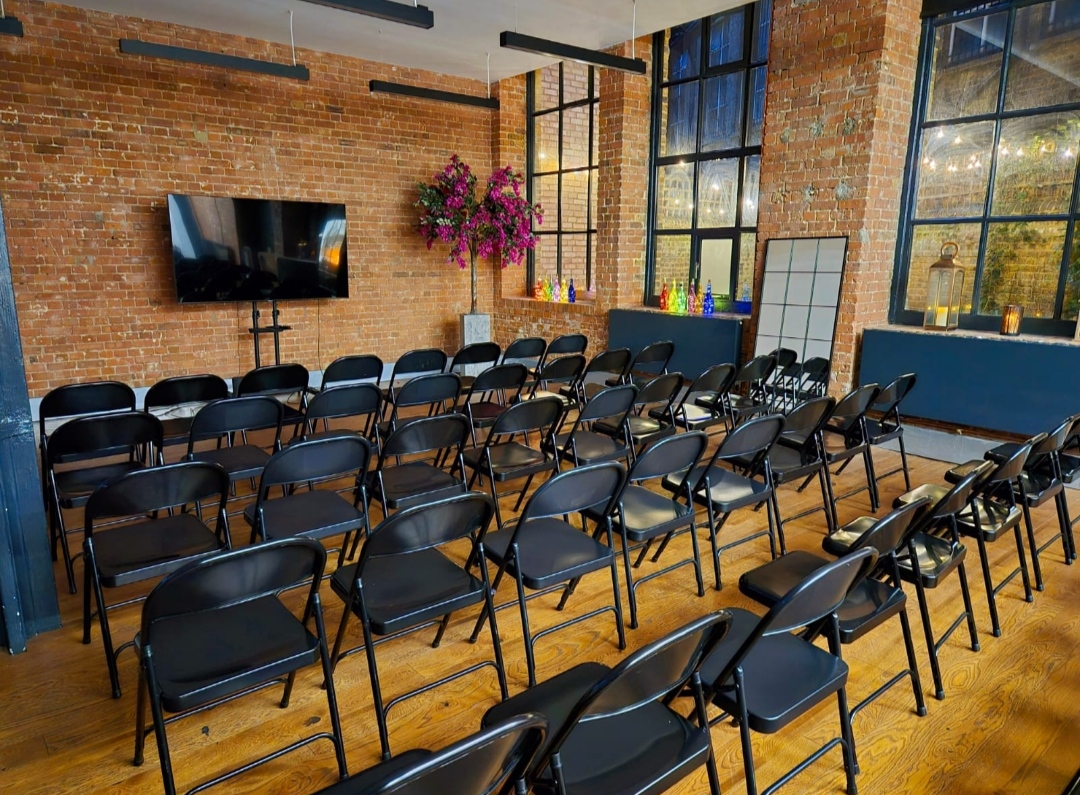 Event space with black chairs, exposed brick, ideal for corporate meetings and gatherings.