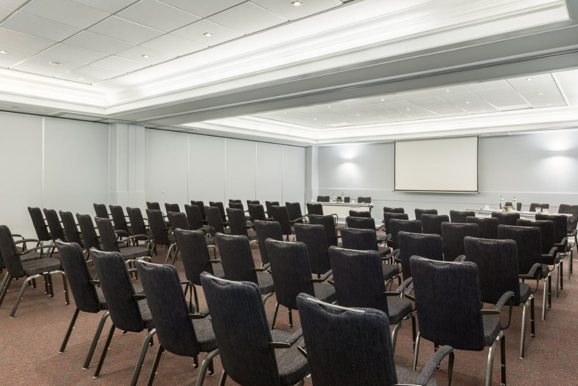 Meeting room setup for conference with aligned chairs and blank presentation screen.
