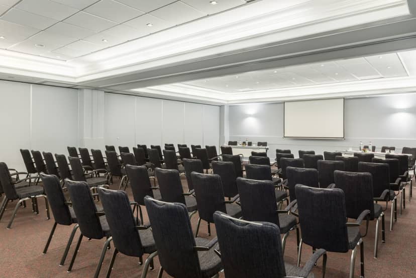 Meeting room setup for conference with aligned chairs and blank presentation screen.