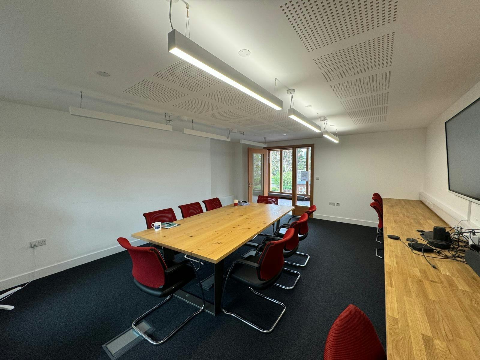 Modern meeting room with wooden table and red chairs, perfect for collaboration events.