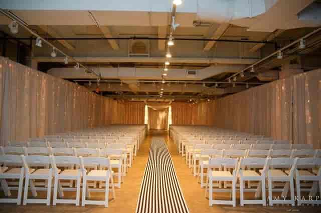 Elegant wedding setup with white chairs and soft lighting in Fashion Industry Gallery.