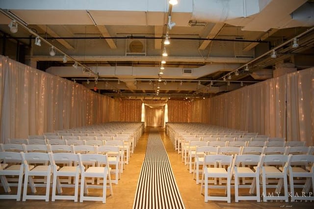 Elegant wedding setup with white chairs and soft lighting in Fashion Industry Gallery.
