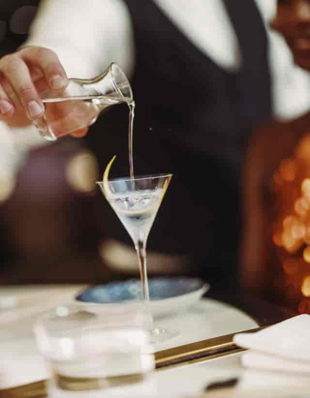Bartender pouring cocktail in martini glass at Harrods Restaurants for upscale events.