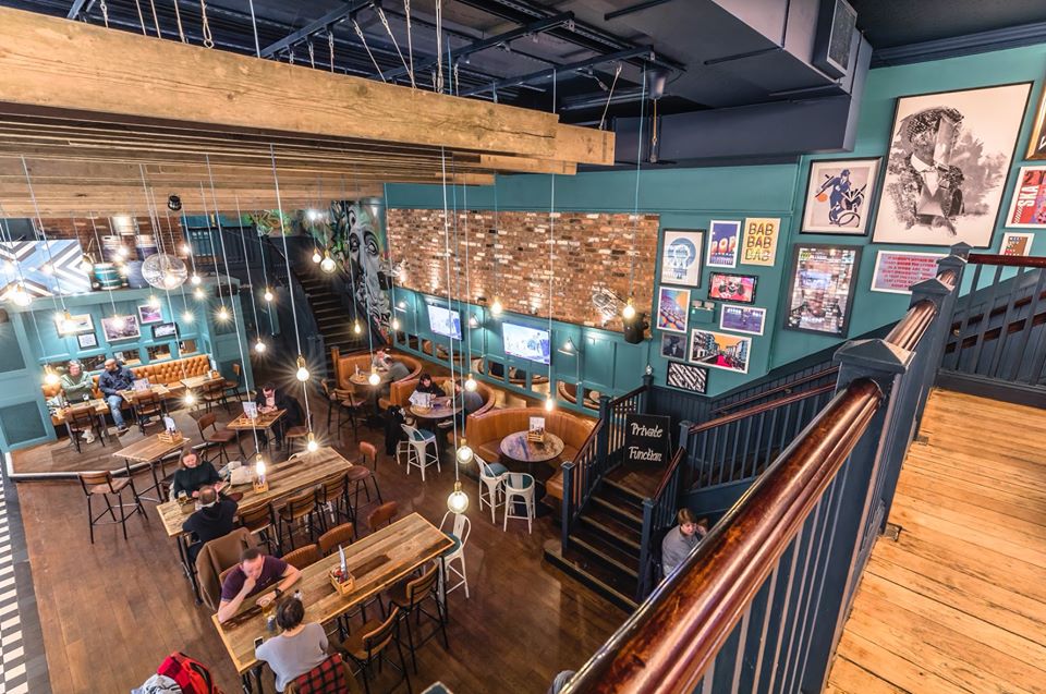 Vibrant multi-level venue with cozy booths for casual meetings and events. - Banner