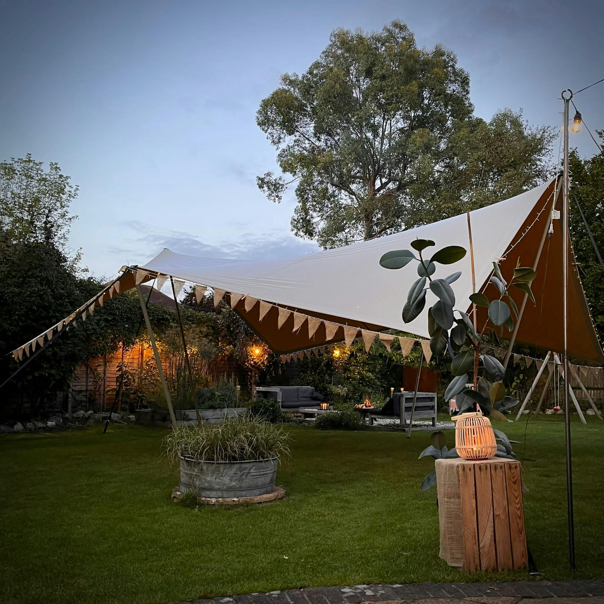 Elegant stretch tent with bunting in a lush outdoor event space for gatherings.