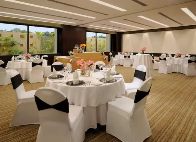 Elegant event space at Hilton Embassy Golf Link Bengaluru with round tables and floral centerpieces.