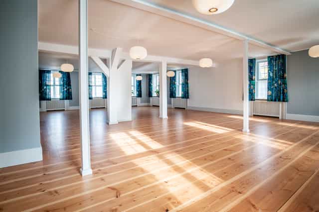 K. Larsen in a spacious, well-lit event space with wooden flooring for gatherings.