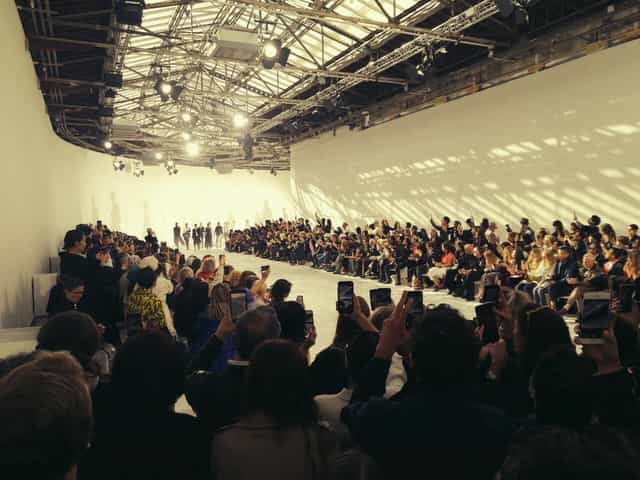 "Fashion runway event at Grande Verrière, Palais de Tokyo with vibrant lighting and engaged audience."