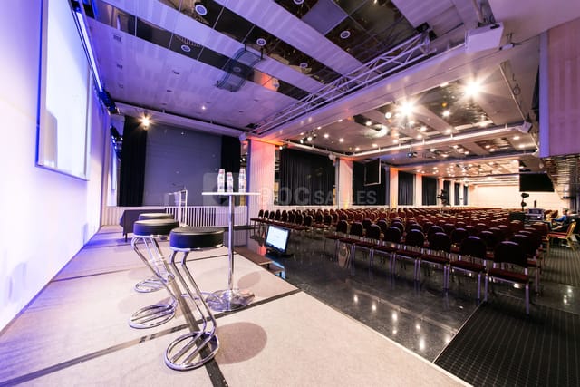 Conference room with stage and AV tech, ideal for seminars and conferences.