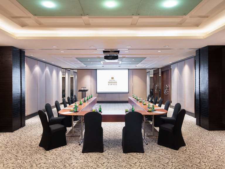 Meeting room with central table and projector screen at Regal Airport Hotel for conferences.