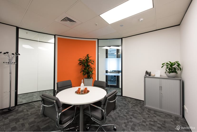 Modern conference room with round table, orange wall, ideal for team meetings.