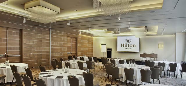 Ballroom at Hilton Milan with round tables for corporate events and conferences.