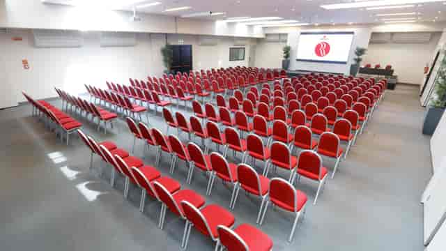 Event space at Ramada Plaza Milano with red chairs for conferences and presentations.