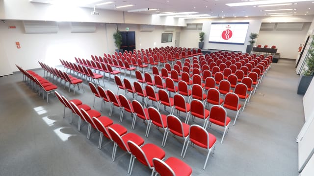 Event space at Ramada Plaza Milano with red chairs for conferences and presentations.