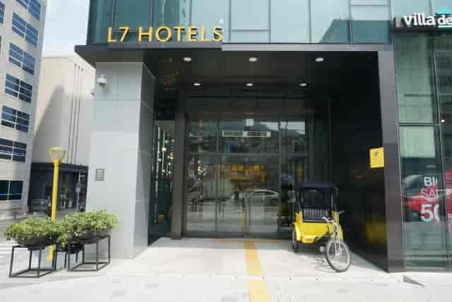 L7 Myeongdong hotel entrance with modern facade and vibrant yellow rickshaw for events.