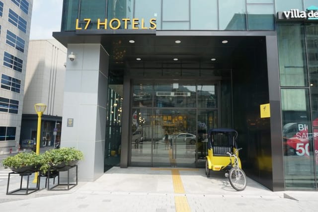 L7 Myeongdong hotel entrance with modern facade and vibrant yellow rickshaw for events.