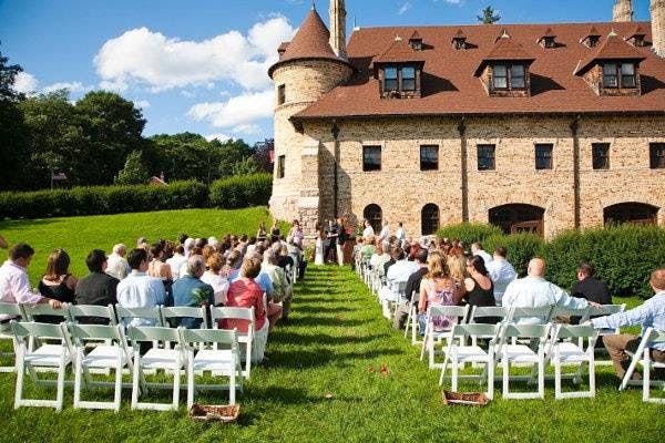 Outdoor wedding ceremony at Larz Anderson Auto Museum with white chairs and lush greenery.