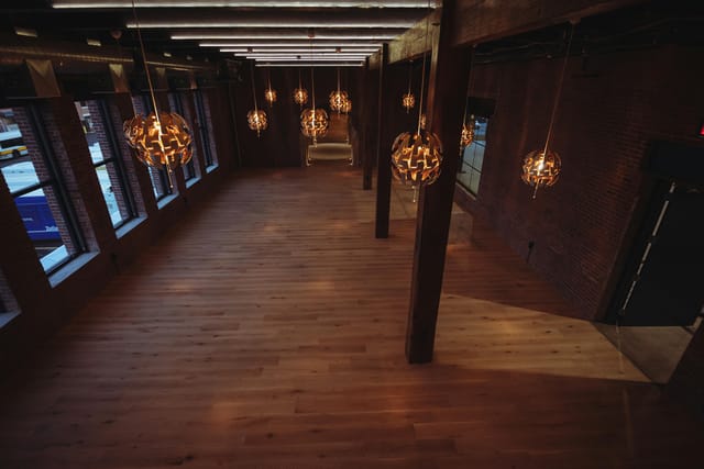 Spacious event venue with wooden flooring and pendant lights, ideal for meetings and gatherings.
