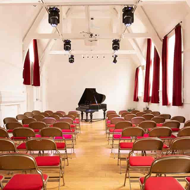 Auditorium with grand piano, brown chairs, ideal for music recitals and workshops.