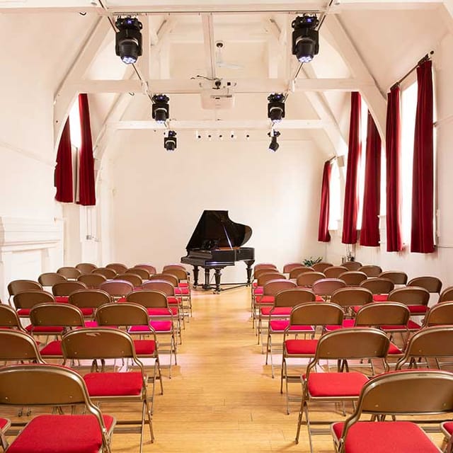 Auditorium with grand piano, brown chairs, ideal for music recitals and workshops.