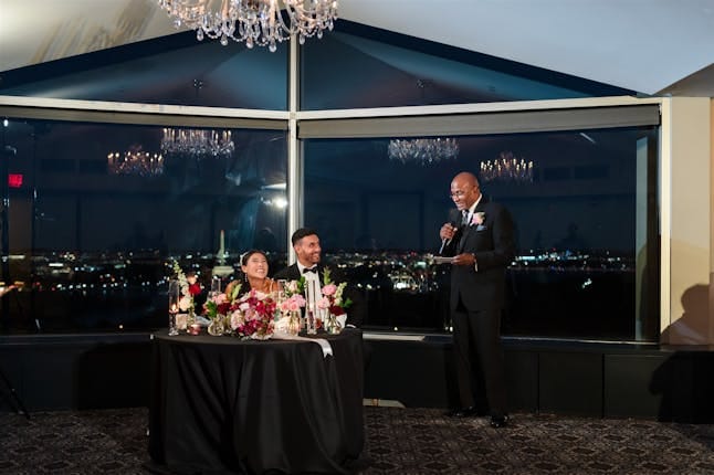 Elegant wedding reception head table on outdoor terrace with city views at night.