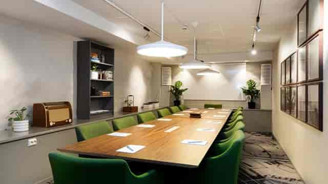 Modern meeting room at Elite Hotel Adlon with wooden table and green chairs for workshops.