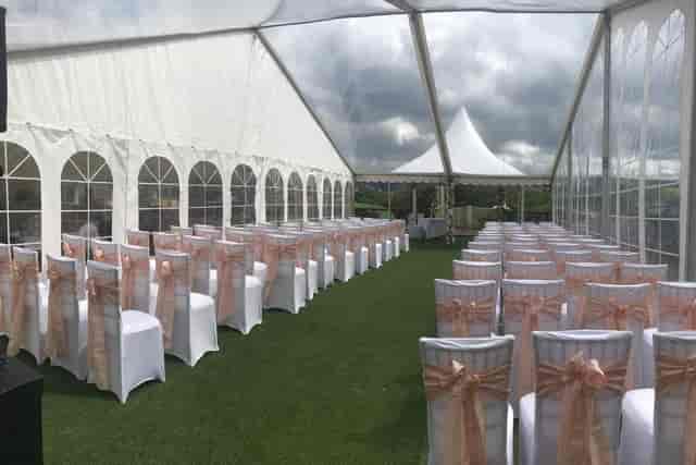 Wedding venue marquee with white chairs and peach sashes, perfect for outdoor events.