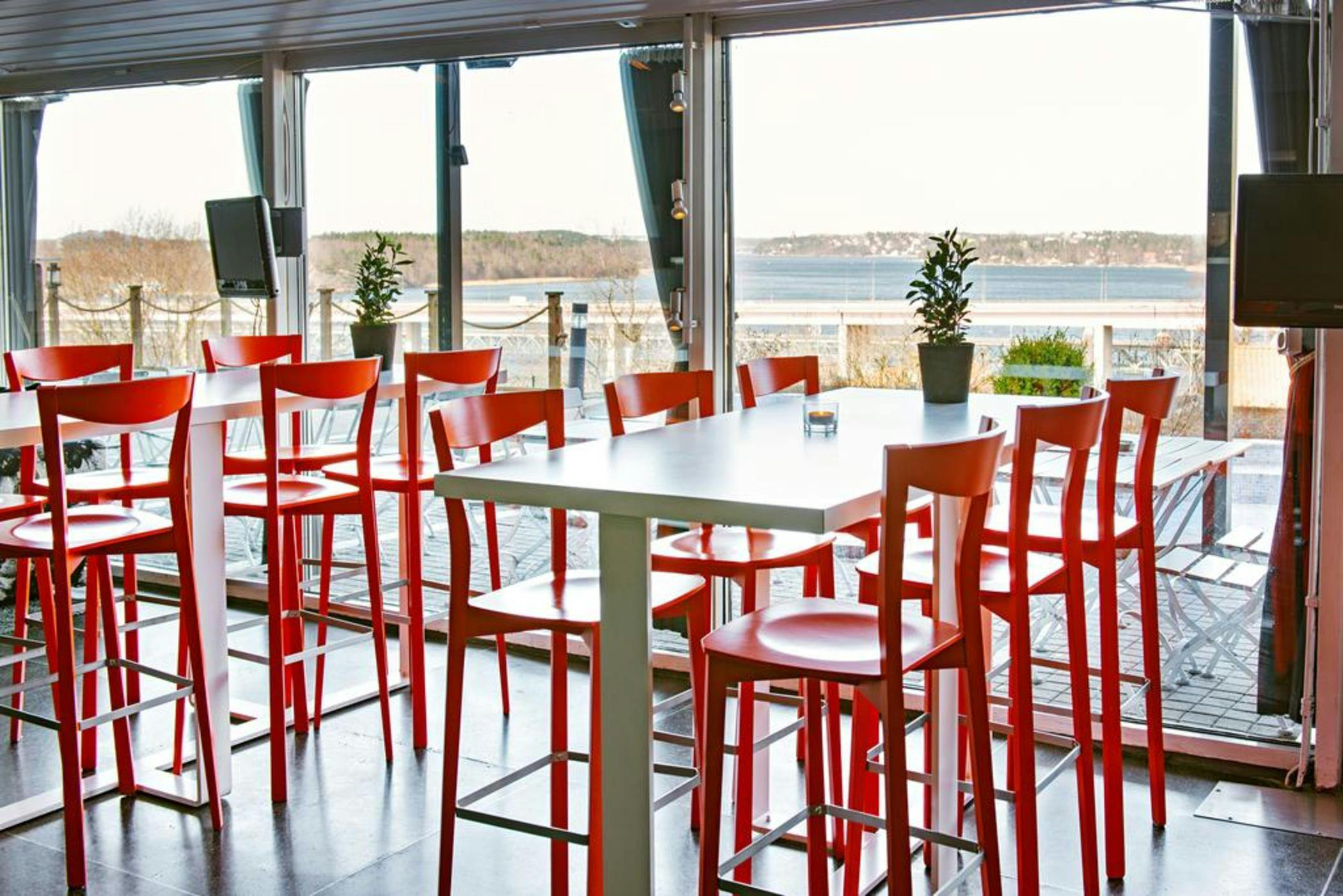 Modern event space with red bar stools and water views, ideal for networking and gatherings.