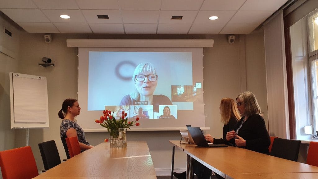 Hybrid meeting setup in IVA Conference Centre with large screen and flowers.