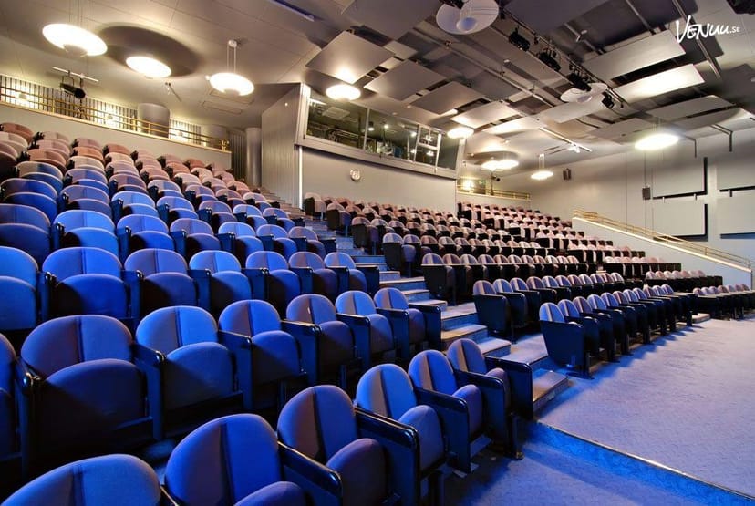 Conference room with tiered seating and blue chairs, ideal for presentations and events.