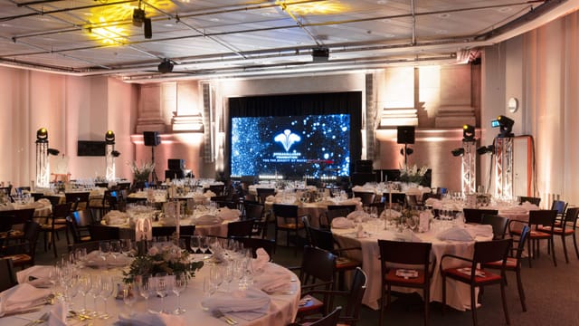 Elegant conference center set for formal dinner with ambient lighting and AV equipment.