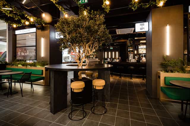 Modern event venue with central bar and greenery, ideal for corporate meetings and social functions.
