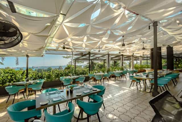 Outdoor dining at Club Matera, featuring elegant draped ceiling and vibrant turquoise chairs.