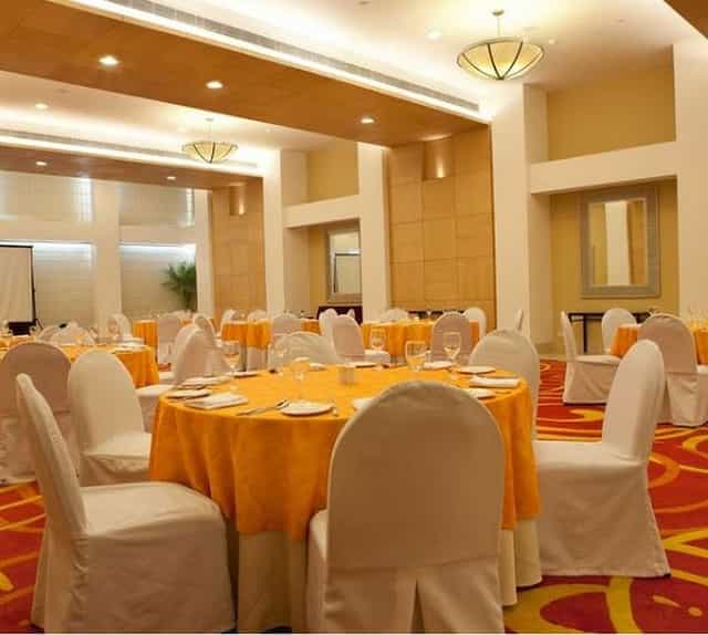 Banquet hall at Lemon Tree Hotel Kaushambi with orange tablecloths for events.
