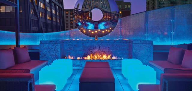 Rooftop bar at The Ritz-Carlton, Chicago with modern seating and vibrant blue lighting.