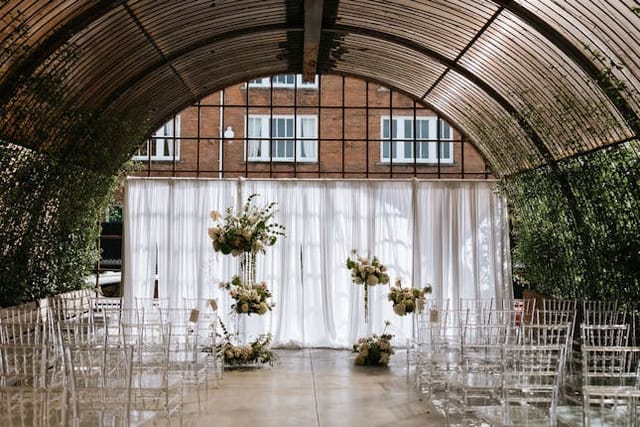 Elegant wedding event space with archway, floral decor, and clear acrylic chairs.