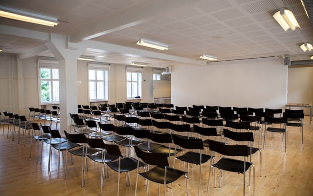Lecture Room at Royal Danish Academy, spacious with black chairs for seminars and presentations.