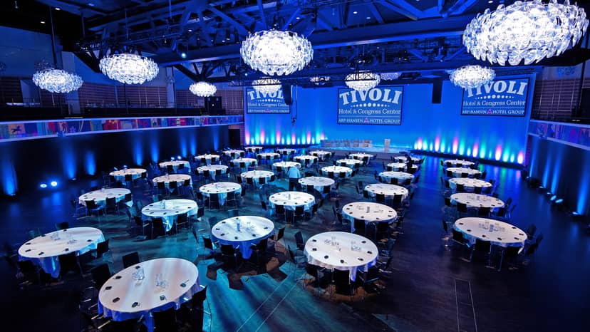Spacious conference venue with round tables and blue lighting at Tivoli Hotel.