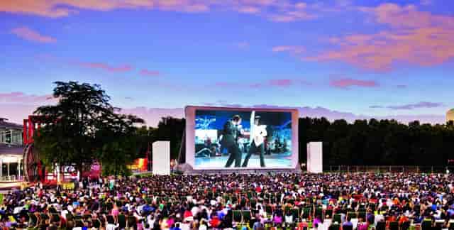 Outdoor film screening at Prairie du Triangle, vibrant audience on green chairs.