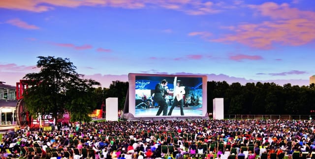 Outdoor film screening at Prairie du Triangle, vibrant audience on green chairs.