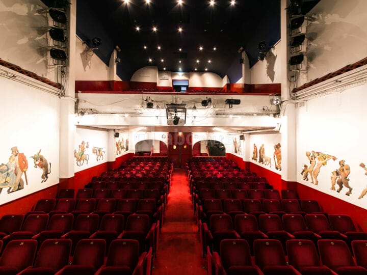 Illuminated Salle des fêtes with tiered red seating for presentations and events.
