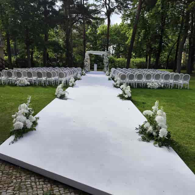 Elegant outdoor wedding setup with floral arch and white aisle at Villa Schützenhof.