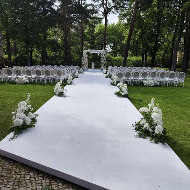 Elegant outdoor wedding setup with floral arch and white aisle at Villa Schützenhof.