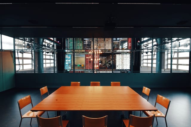 Modern meeting room with wooden table, natural light, for collaboration and workshops.
