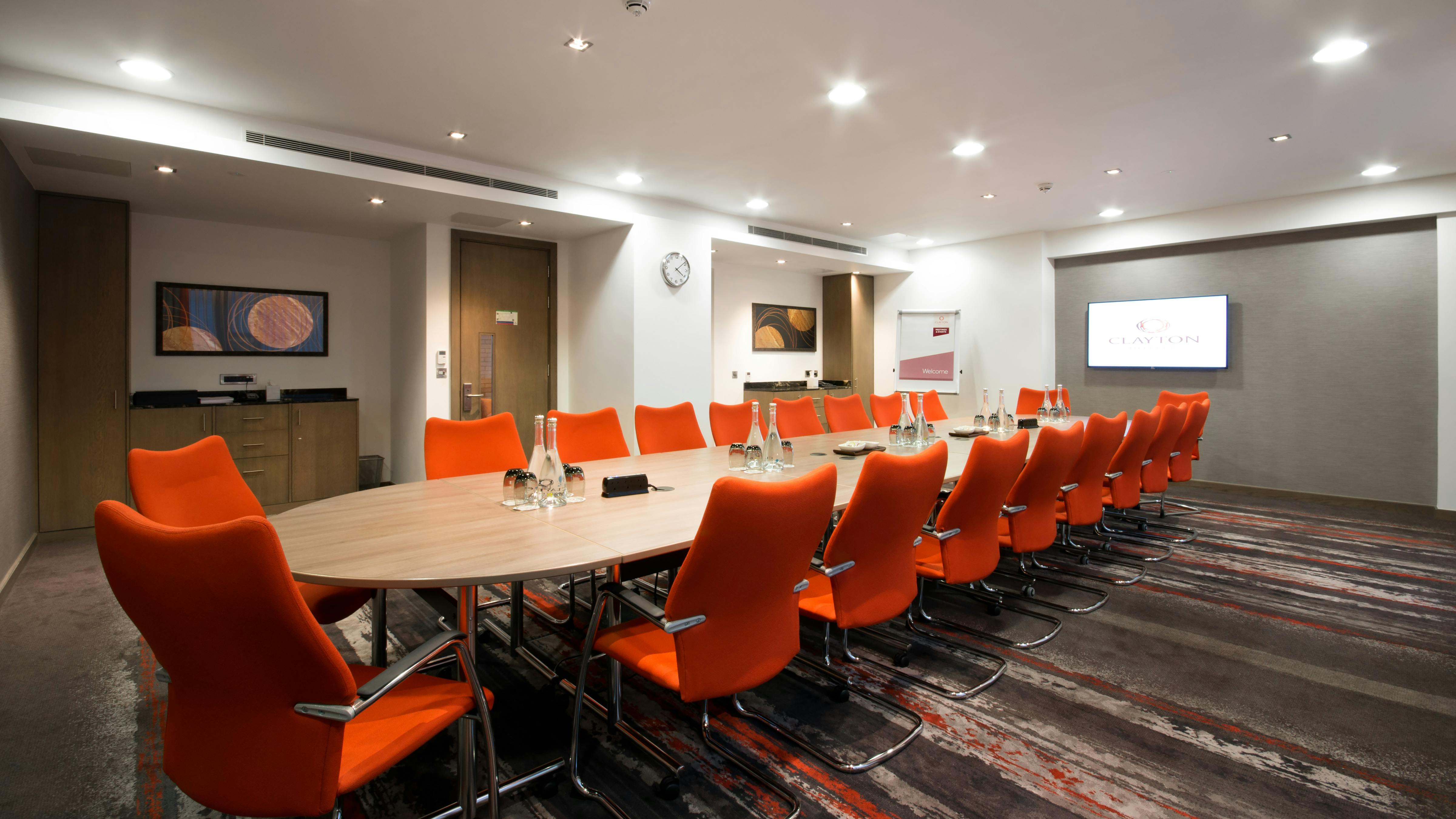 Gunnersbury Suite meeting room with oval table and orange chairs, perfect for conferences.