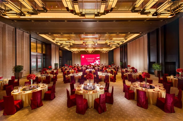 Elegant conference hall banquet setup with red and gold decor for corporate events.