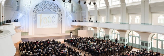 Elegant lecture hall at a conference with high ceilings and an engaged audience.