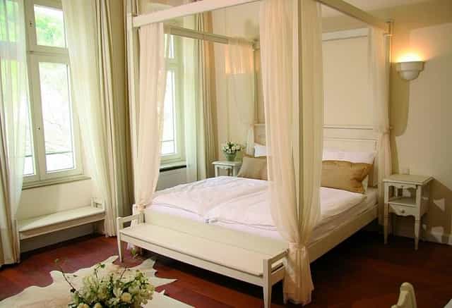 Four-poster bed in serene Hotel Villa Marstall room for retreats and gatherings.