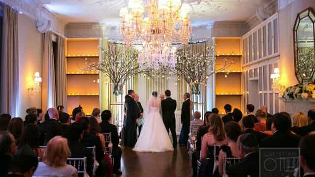 Elegant wedding ceremony in grand ballroom with chandeliers and floral decor.